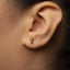 A close-up of a person's ear with a small gold-colored key earring in the earlobe.