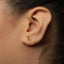 A close-up of a person's ear with a small gold earring featuring a leaf design.