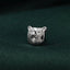 A close-up image of a silver bear head pin resting on a textured green fabric.