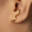A close-up of a person's ear with a gold snake-shaped earring attached.