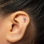 A person's ear with a small silver cocktail glass-shaped earring inserted in the earlobe.