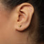 A close-up view of a person's ear adorned with a small gold earring featuring a small bird-like design.