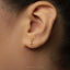 A close-up of a person's ear wearing a small gold-colored earring shaped like a martini glass.