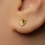 A close-up view of a person's ear with a small gold-colored earring featuring a shield-like design.