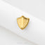 A close-up image of a gold-colored shield-shaped object, possibly a pin or badge, resting on a white fabric surface.