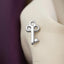 A silver key-shaped pin is displayed on a white fabric surface.