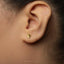 A close-up view of a person's ear with a small gold-colored earring featuring a shield-like design.