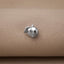 A small silver charm in the shape of a leaf is resting on a beige fabric surface.