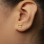 A close-up of a person's ear wearing a gold-colored earring shaped like a sewing machine.