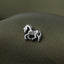 A small silver metal horse pin is resting on a textured fabric surface.