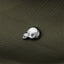 A silver metal object resembling a skull or a similar head shape is placed on a textured green fabric.