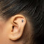 A close-up of a person's ear with a small, silver earring in the earlobe.