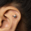 A silver earring in the shape of a small bird is visible in the image.