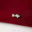 A silver earring with a white gemstone is resting on a red fabric surface.