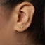 A close-up of a person's ear with a small gold earring featuring a small gemstone.