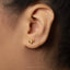 A close-up of a person's ear wearing a small gold-colored earring with a small animal-shaped charm.