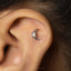 A close-up of a person's ear with a silver crescent moon-shaped earring with a small white stone in the center.