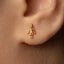 A close-up of a person's ear wearing a small gold-colored earring with a small figure on it.