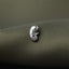 A close-up image of a silver earring or brooch resting on a textured fabric surface.