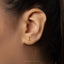 A close-up view of a person's ear with a small gold earring featuring a moon-like design.