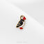 A small, colorful bird-shaped pin or badge with a black and white body, red beak, and feet, placed on a white surface.
