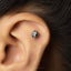 A close-up of a person's ear with a small, ornate earring in the earlobe.