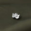 A silver pin with a mask design is resting on a textured fabric surface.