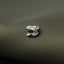 A close-up image of a small, silver-colored metal object resembling a dinosaur head or skull, resting on a textured green fabric.