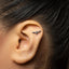 A close-up of a person's ear with a small silver earring in the shape of a bat resting on the earlobe.