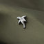 A close-up image of a small, metallic flower-shaped pin or badge resting on a textured, green fabric surface.