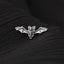 A silver bat pin is resting on a black fabric surface.