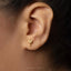 A close-up of a person's ear wearing a small gold earring shaped like a palm tree.
