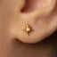 A close-up of a person's ear with a small gold earring featuring a star-shaped gemstone.