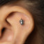 A silver earring with a small acorn-shaped charm is visible in the person's ear.