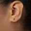 A close-up of a person's ear with a small gold earring in the earlobe.