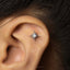 A close-up of a person's ear with a small, intricate earring featuring a sun-like design and a white stone or gemstone at its center.