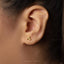 A close-up of a person's ear with a small gold earring featuring a spiral design.