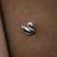 A small silver swan figurine is resting on a textured brown surface.