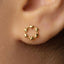 A close-up view of a person's ear adorned with a small gold earring featuring a circular design.