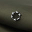 A silver ring with a circular design of small stars is resting on a textured fabric surface.