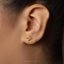 A close-up view of a person's ear with a small gold earring featuring a geometric design.