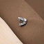 A close-up image of a small, silver-colored object, possibly a piece of jewelry, resting on a textured brown surface.