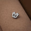 A small, silver, metal object with a unique, abstract design is resting on a textured, brown surface.