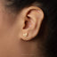 A close-up view of a person's ear adorned with a small gold earring featuring a heart-shaped design.