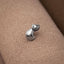 A small silver cat-shaped earring is resting on a textured beige surface.