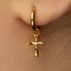 A close-up of a person's ear wearing a gold-colored earring with a small cross-shaped charm hanging from it.