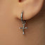 A close-up of a person's ear with a silver cross-shaped earring hanging from the earlobe.
