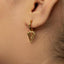 A close-up of a person's ear wearing a gold-colored earring with a triangular pendant.