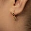 A close-up view of a person's ear wearing a gold-colored earring with an octopus charm hanging from it.