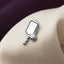 A silver pin with a tennis racket and ball attached to it, resting on a white fabric surface.